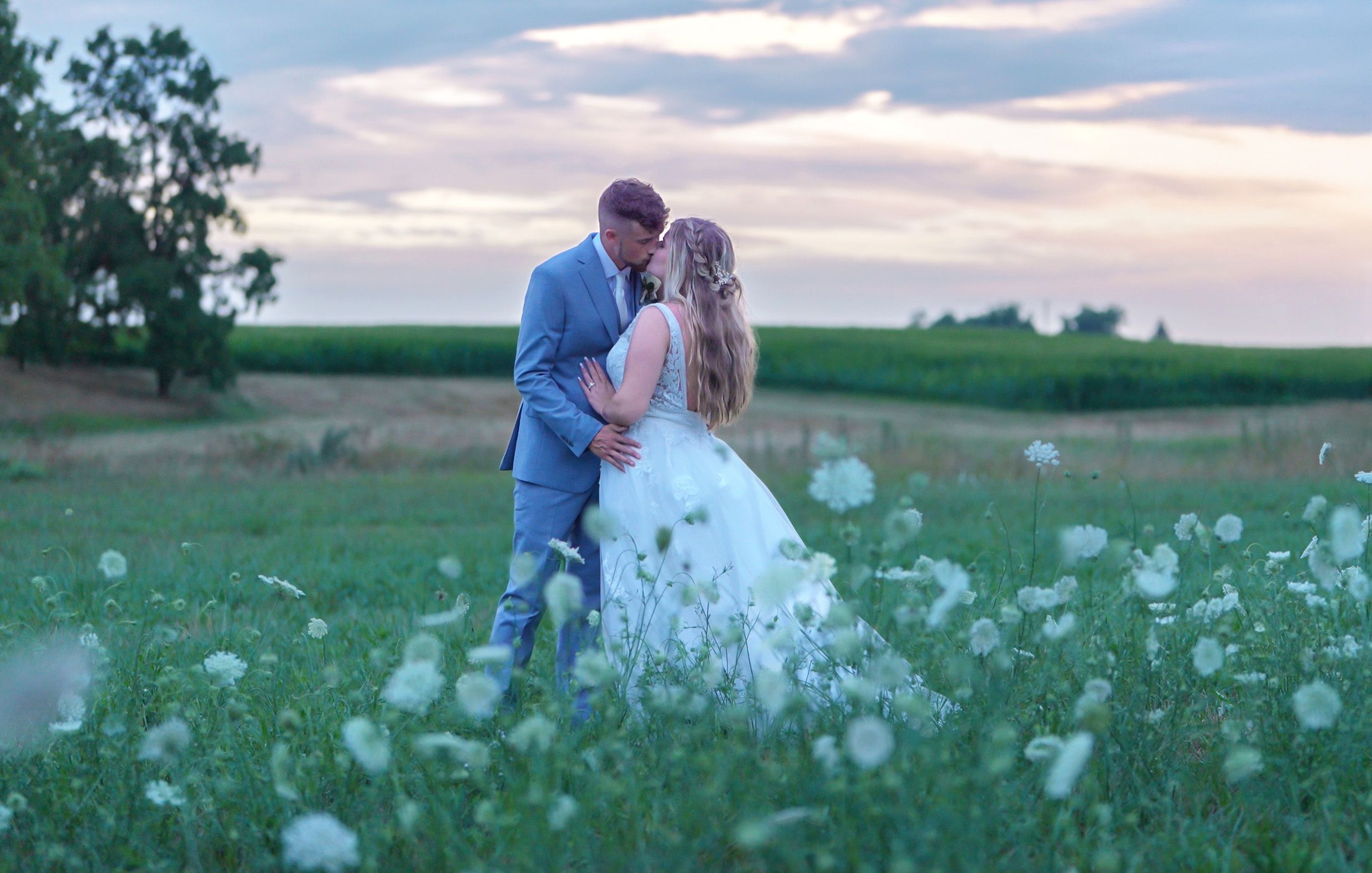Bride and groom share a romantic kiss in a wildflower field at sunset on their wedding day.