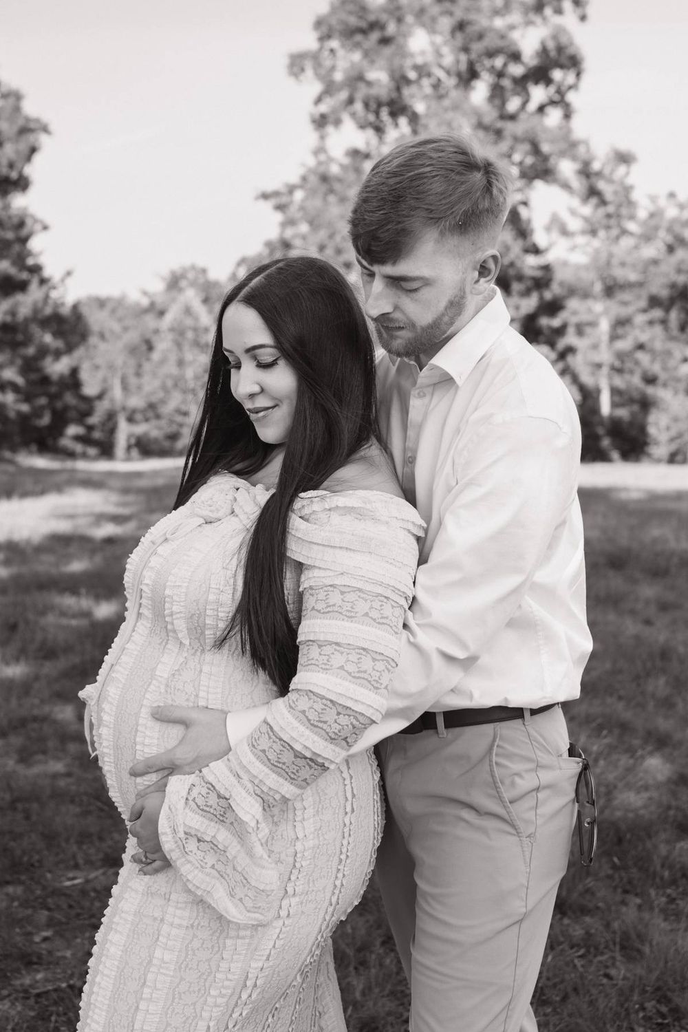 Black and white photo of a couple embracing outdoors, with the woman visibly pregnant Asheboro NC