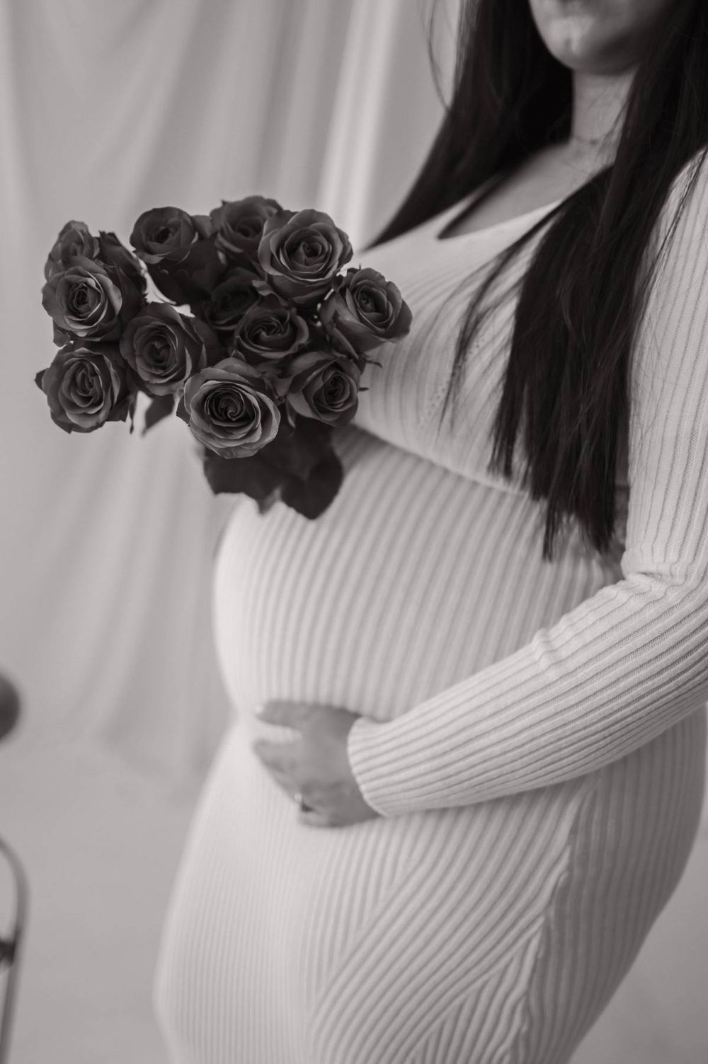 Black and white photo of pregnant woman in ribbed dress holding roses while cradling baby bump High Point NC
