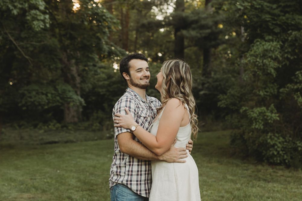 Couple embracing and smiling at each other in a lush green backyard with string lights at dusk.