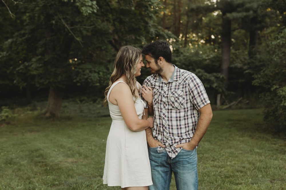Couple sharing a romantic moment outdoors in a lush green park, woman in white dress and man in plaid shirt.