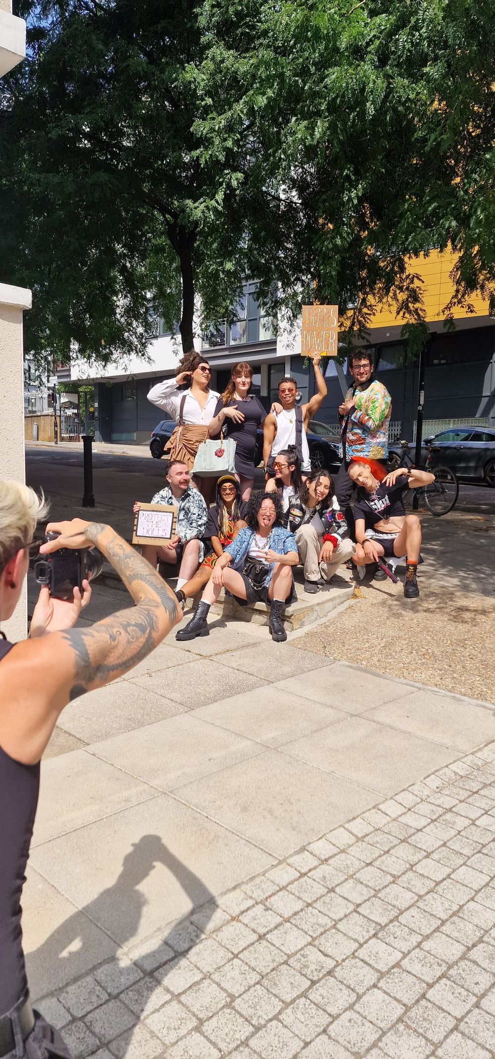 Group of protesters posing for a photo on a sunny urban street holding signs.