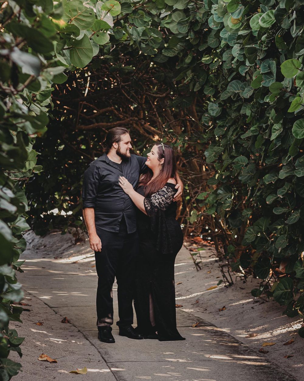 Couple in black outfits sharing a romantic moment under a lush green leafy archway on a garden path at Blowing rocks beach Jupiter.