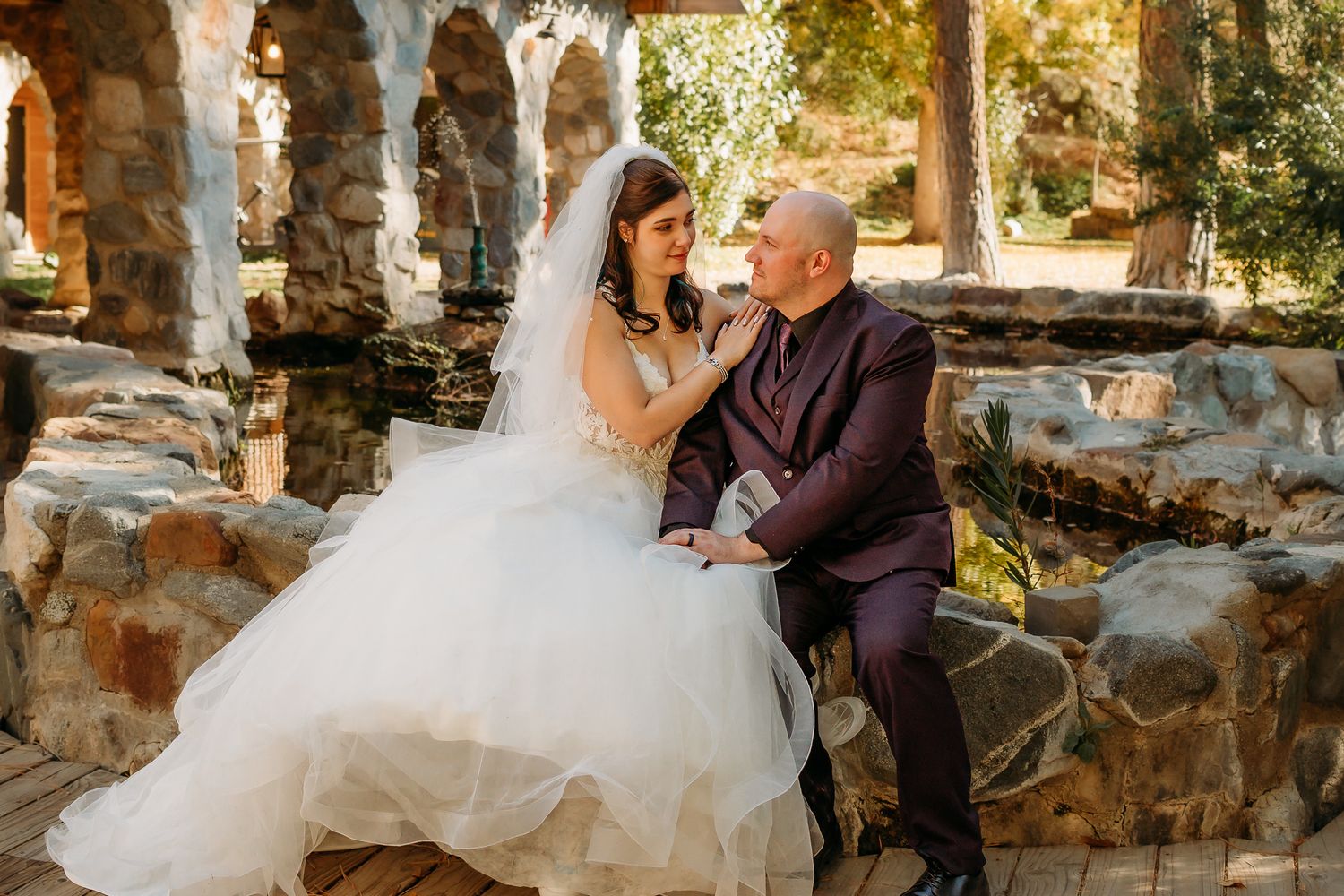 Joyful newlyweds celebrating at wedding reception, bride in white lace wearing heart sunglasses, groom in burgundy vest laughing.