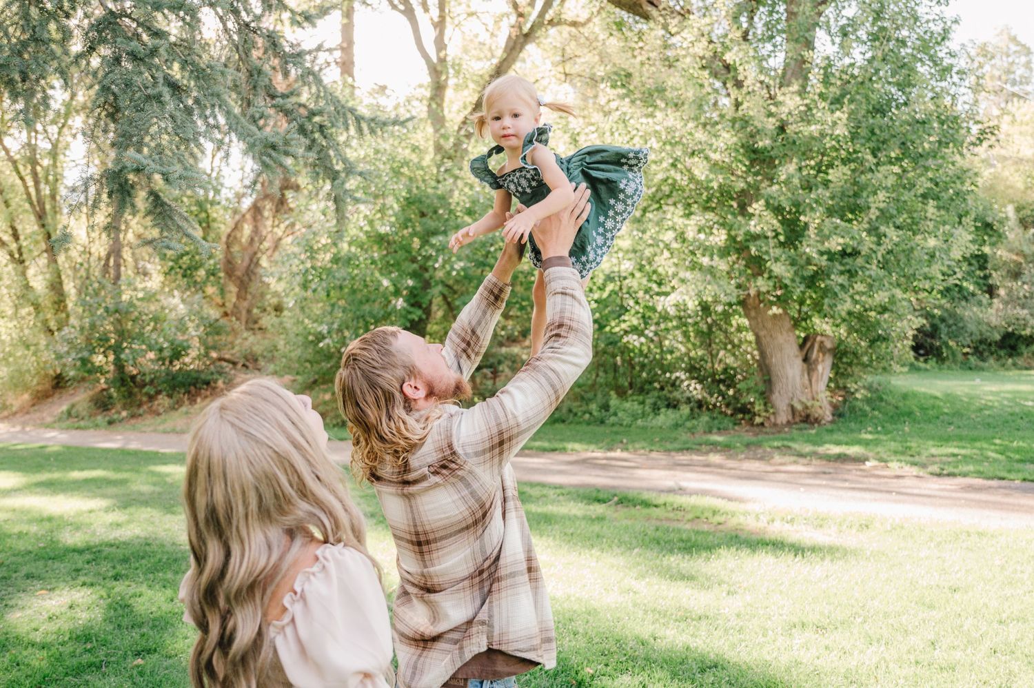 Family enjoying a playful outdoor moment in a park on a sunny day with green trees in the background.
