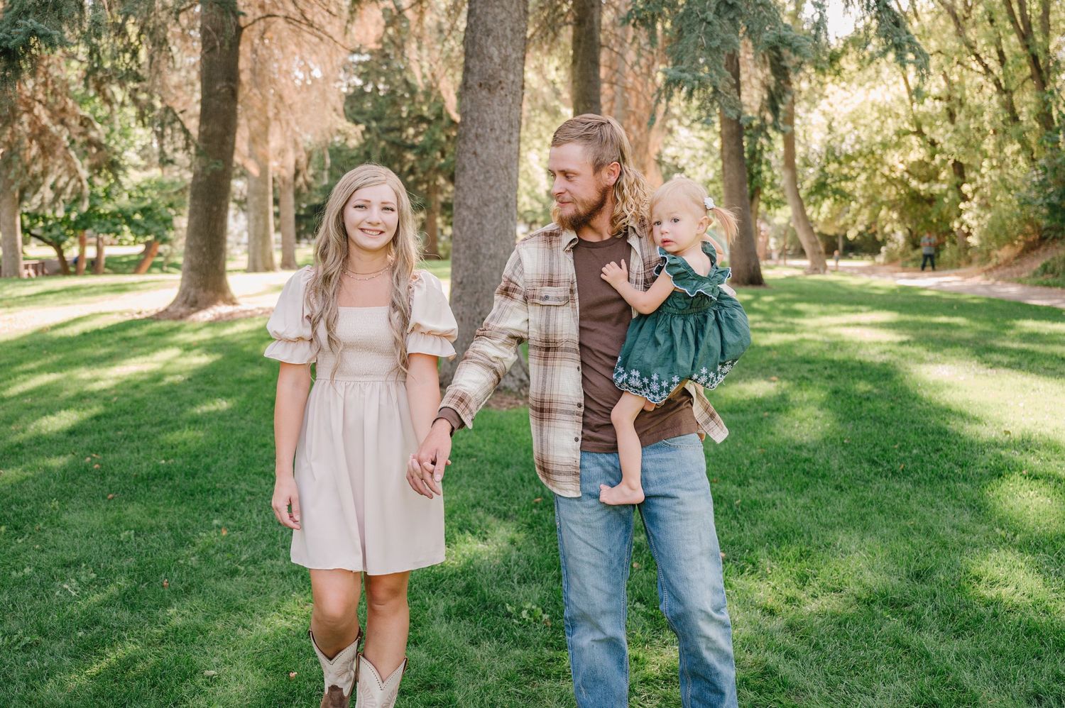 A family walks together outdoors on a sunny day in a grassy park with trees in the background.