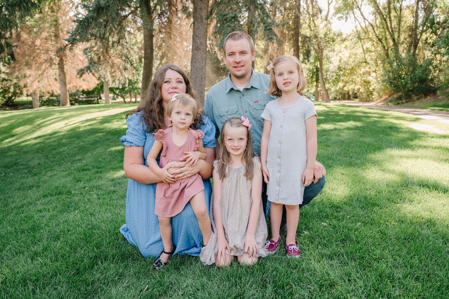A family wearing coordinated pink and blue outfits poses together on a sunny lawn with trees in the background.
