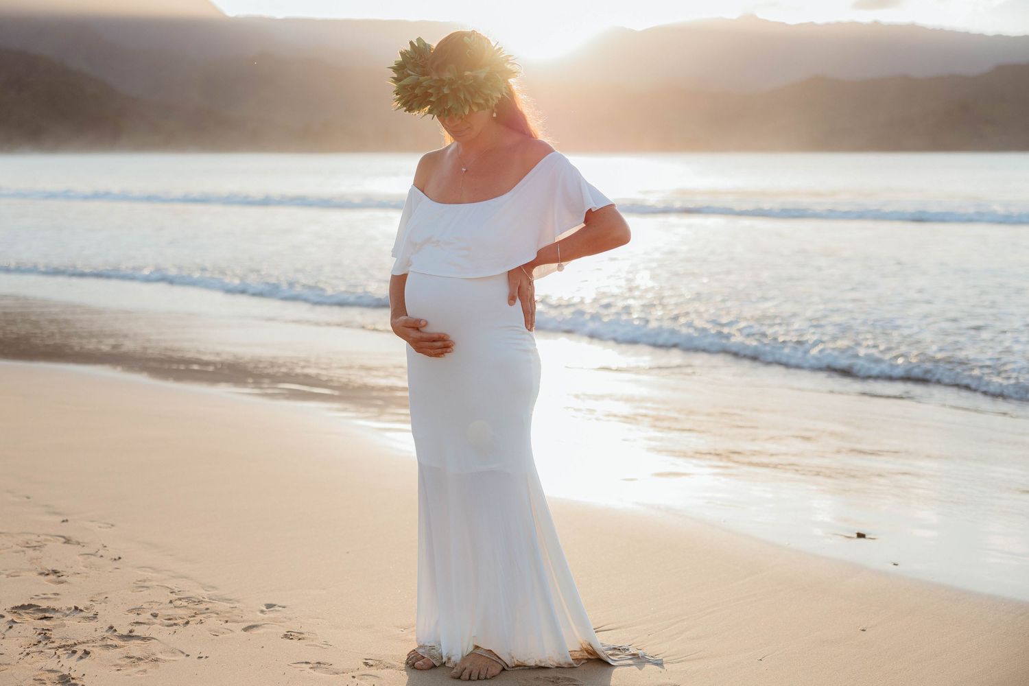 Sunset maternity session in Hanalei Bay, Kauai with the sun setting along the mountains and ocean in the backdrop.