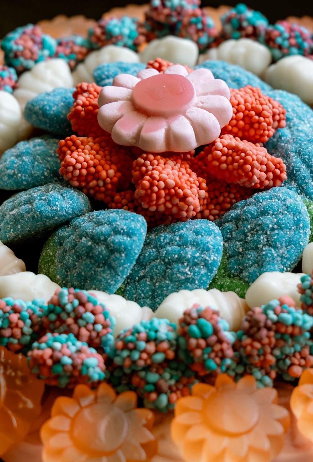 Colorful candy arrangement with blue sugar gummies, pink flower, orange and teal sprinkled sweets in a decorative display.