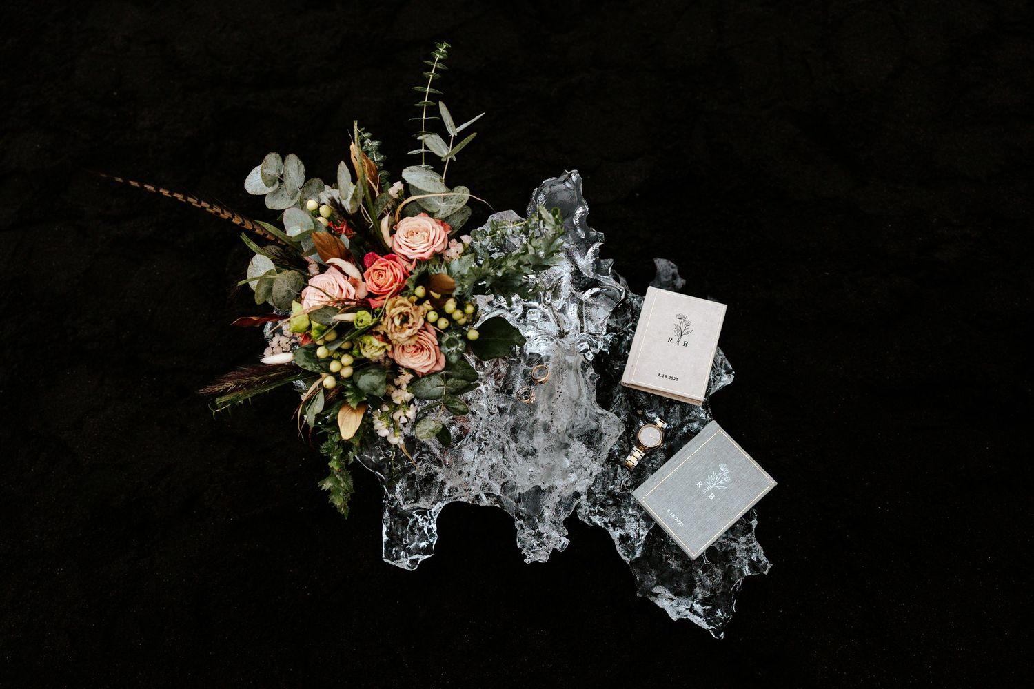 detail photo of elopement bouquet, wedding rings, vow books, and watch on a big piece of glacial ice at Diamond Beach, Iceland
