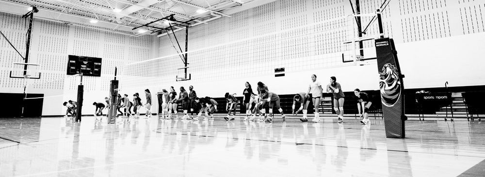 Black and white panoramic photo of a volleyball practice session in a school gymnasium.