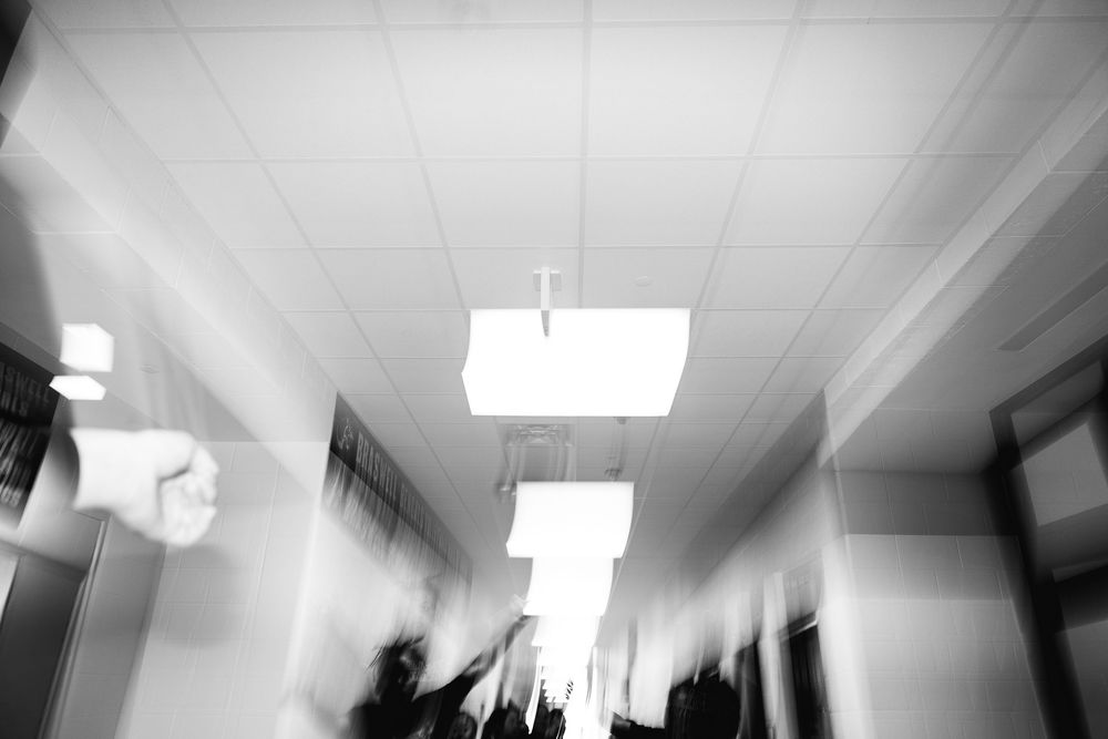 Black and white blurred motion shot of people walking through a school hallway.