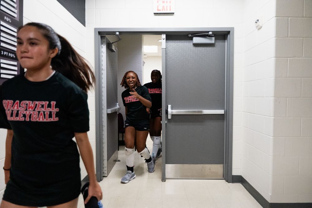 High school volleyball players entering gymnasium through double doors before a match.