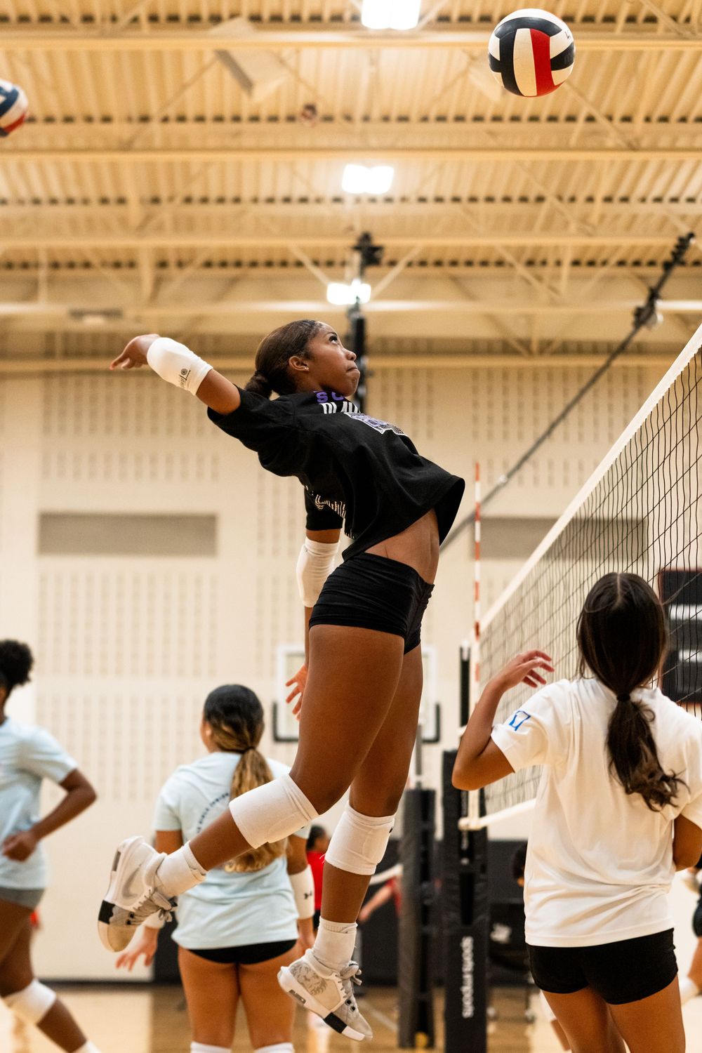 Female volleyball player jumping to spike the ball over the net during practice.