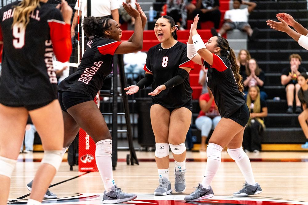 Female volleyball team celebrating a point with player number 8 cheering on court.