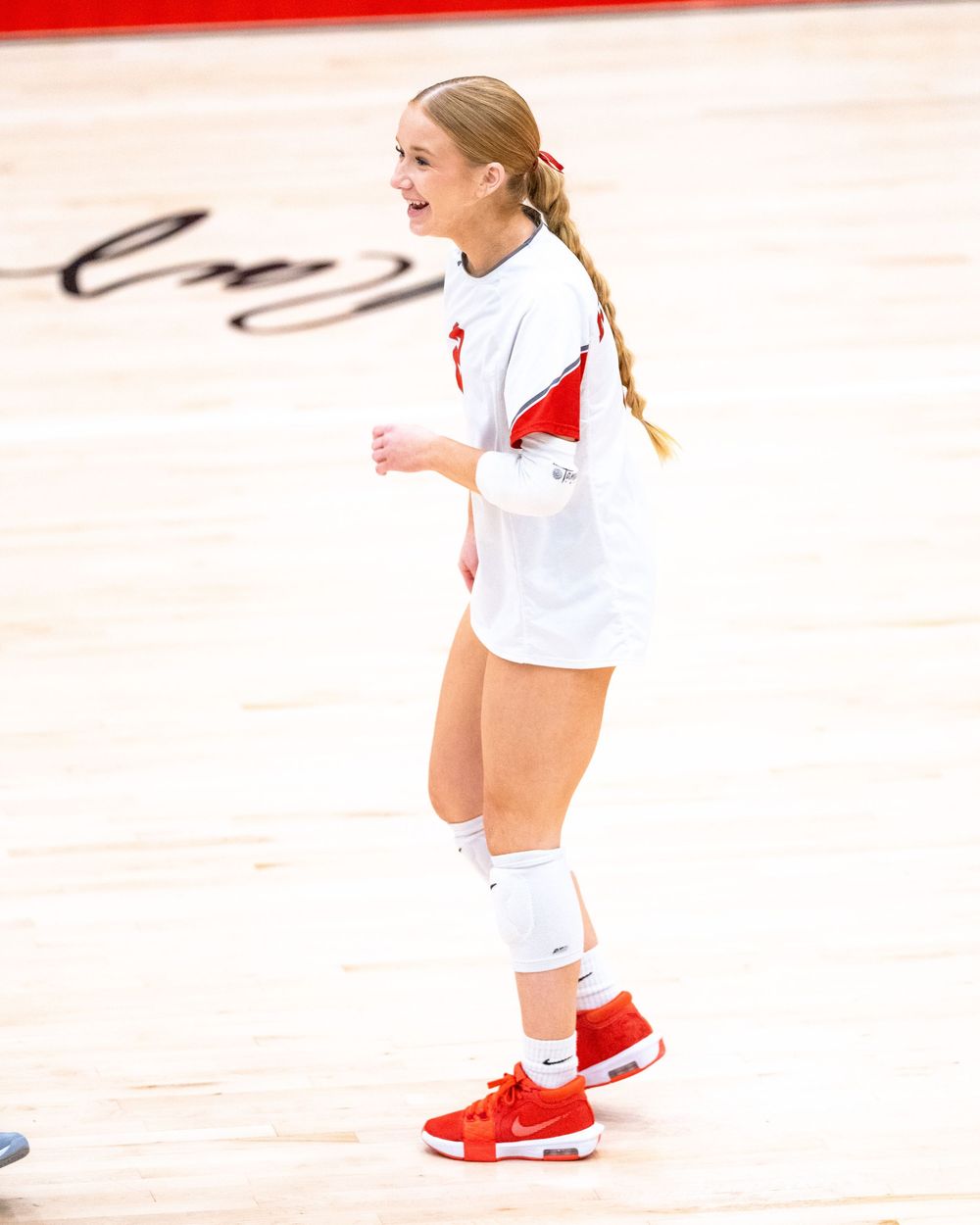 Smiling female volleyball player in white and red Nike uniform standing on court.