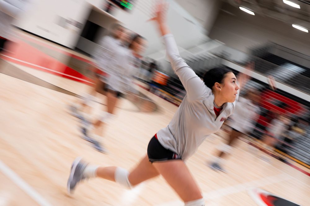 Motion blur action shot of female volleyball player serving during an indoor match.