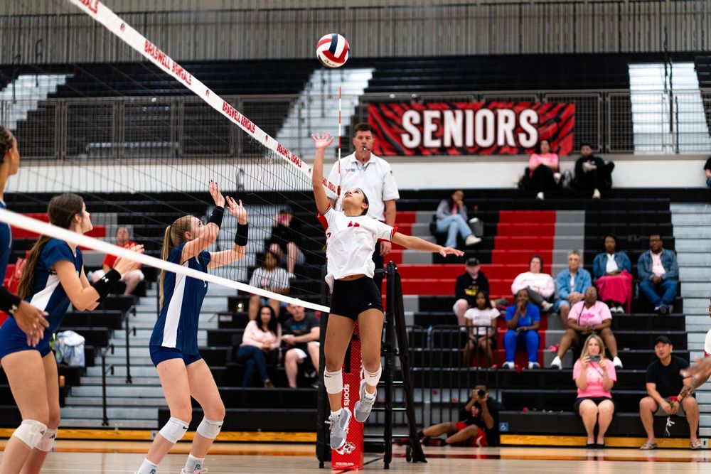 A volleyball player jumps high to spike the ball over the net during a high school match.