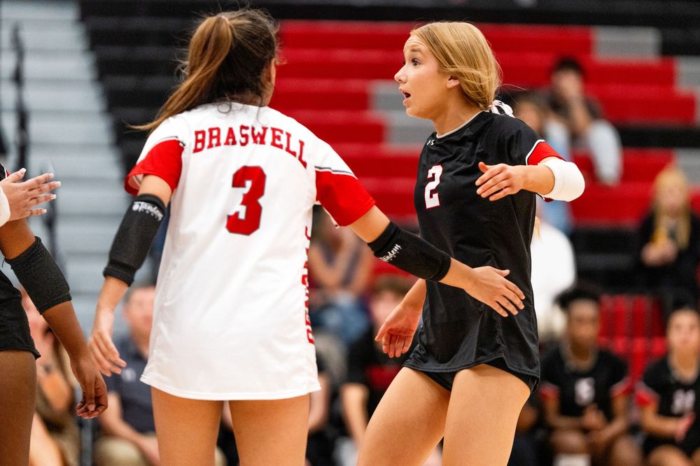 Two Braswell volleyball players exchange a high-five during a competitive high school game.