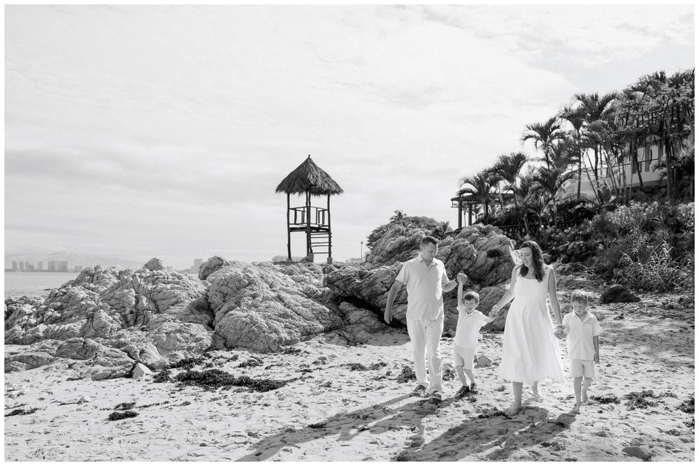 Beach Photo Session at Conchas Chinas Beach in Puerto Vallarta with parents and their sons beside a rustic gazebo and tropical palm trees.