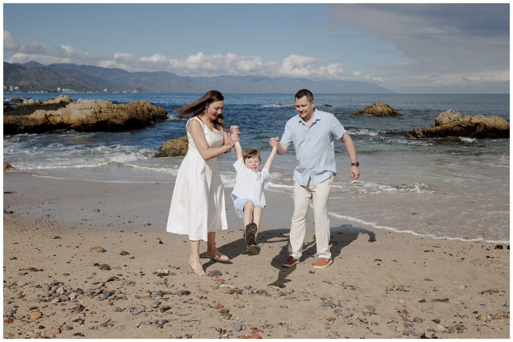 Family Photoshoot at Conchas Chinas Beach in Puerto Vallarta with parents joyfully swinging their toddler along the sunny shoreline.