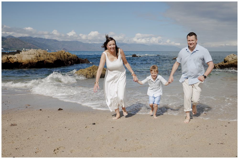 Family Beach Photos at Conchas Chinas Beach in Puerto Vallarta with parents joyfully running hand in hand with their son along the shoreline