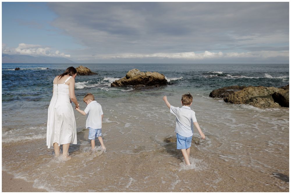 Beach Photo Session at Conchas Chinas Beach in Puerto Vallarta with a mother in a white dress walking beside her two sons in the ocean.