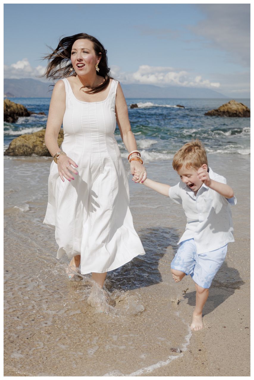 Family Portraits at Conchas Chinas Beach in Puerto Vallarta with a mother and her son joyfully running hand in hand along the shoreline.