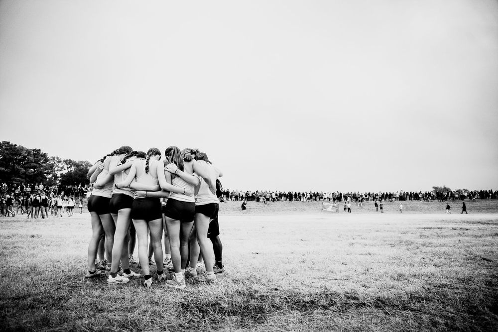 Girls cross country team huddles together in black and white photo at meet.