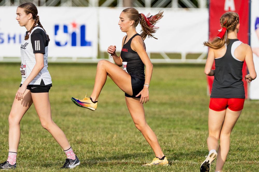 Female athletes performing high knee warm-up drills on a grass field at a UIL cross country meet.