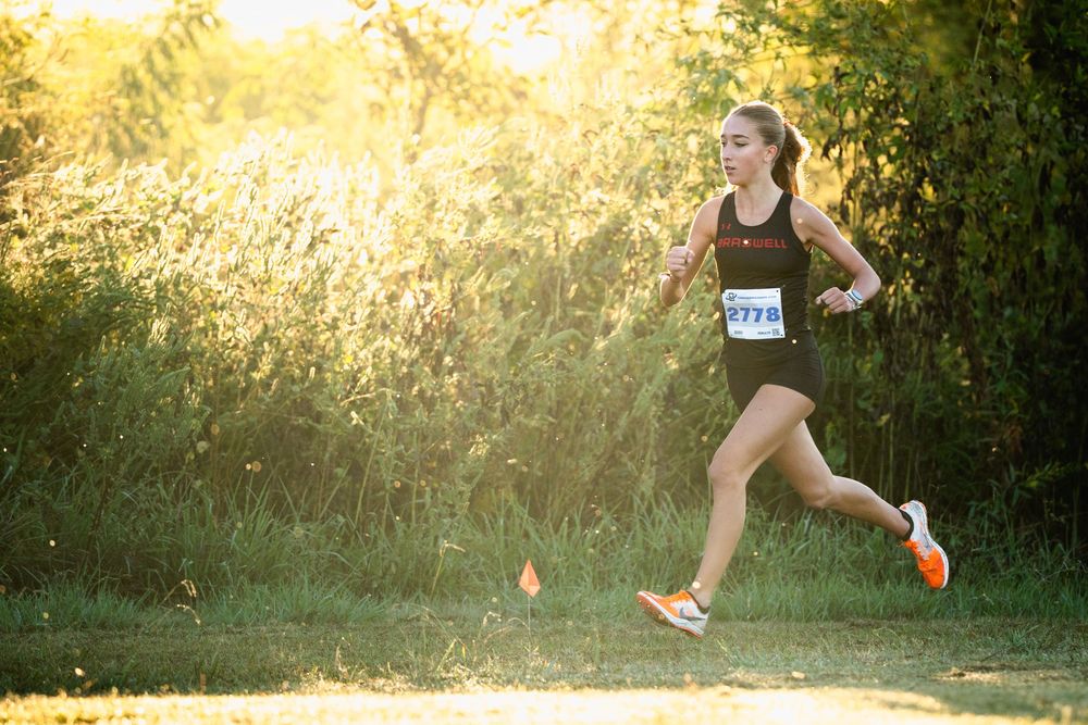 Female cross country runner wearing bib 2778 racing on a sunlit trail surrounded by golden foliage.