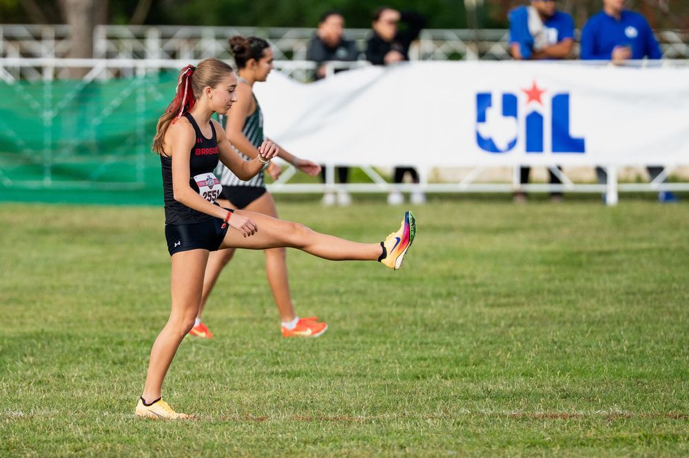 Two female cross country runners competing on grass at a UIL championship meet.