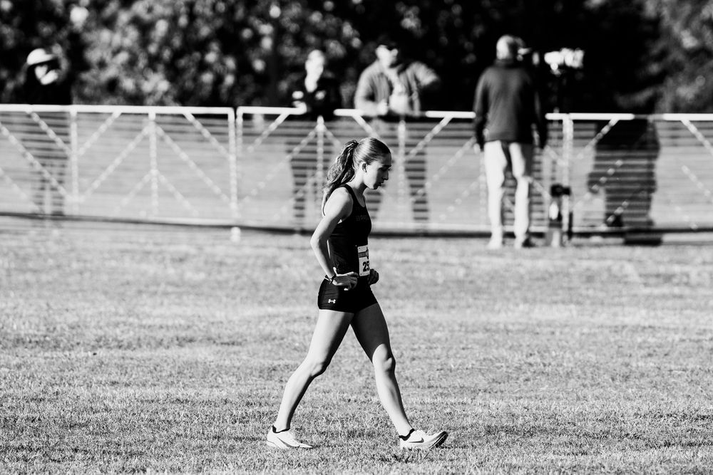 Black and white photo of a female athlete walking across a grass field at a cross country meet.