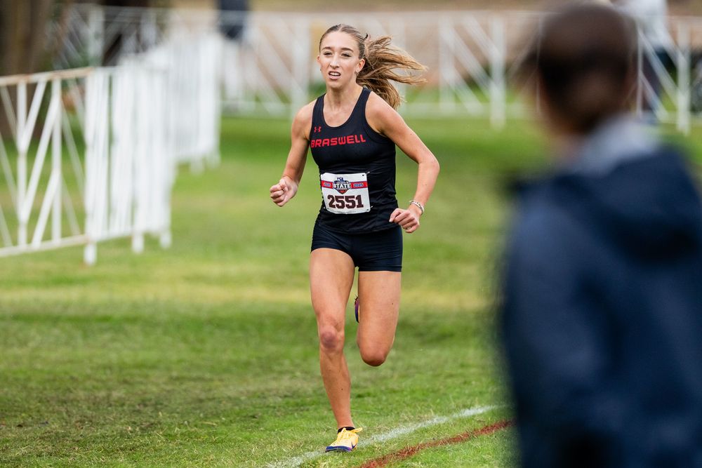 Female cross country runner wearing bib 2551 competes in a race on a grass course.