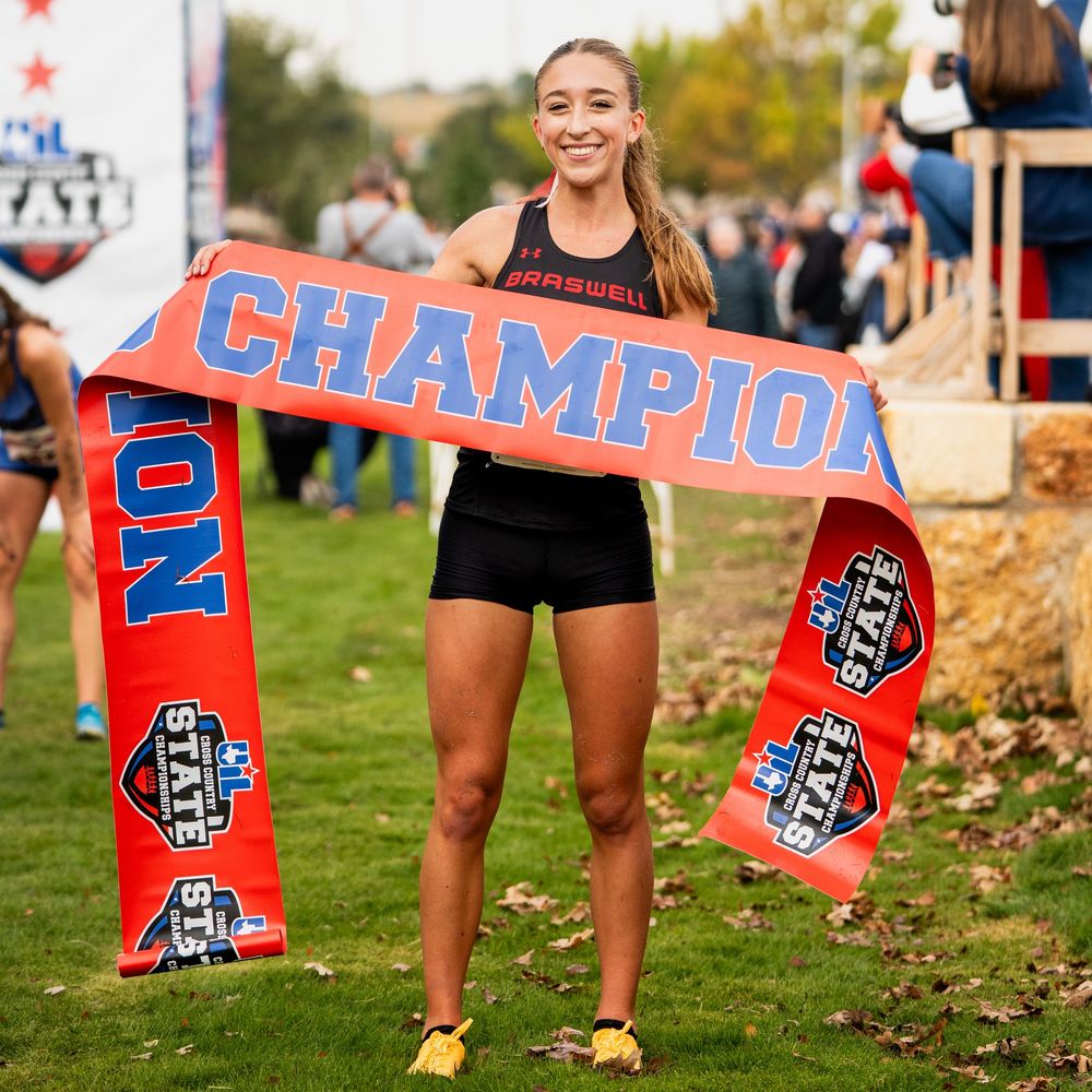 Smiling athlete holds a red Champion banner at a state cross country championship event.