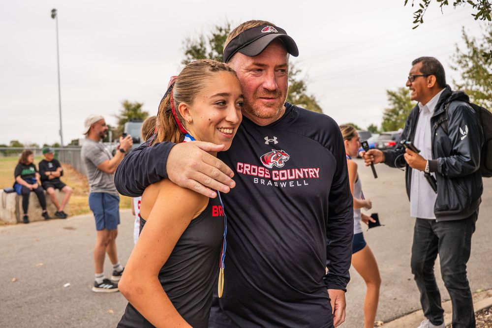 Young female athlete embraces her cross country coach after a competition.
