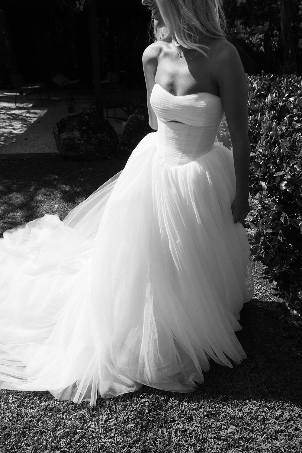 Black and white photo of a bride in a strapless tulle ball gown wedding dress standing outdoors.
