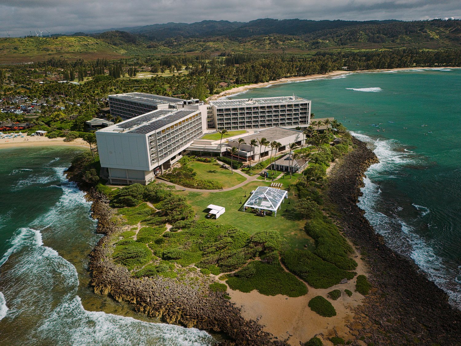 Aerial view of a luxury beachfront hotel on a lush green peninsula surrounded by turquoise ocean waters.
