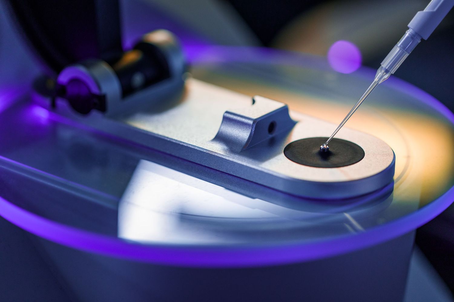 Close-up of a precision needle instrument over a scientific sample disk in a high-tech laboratory setting.
