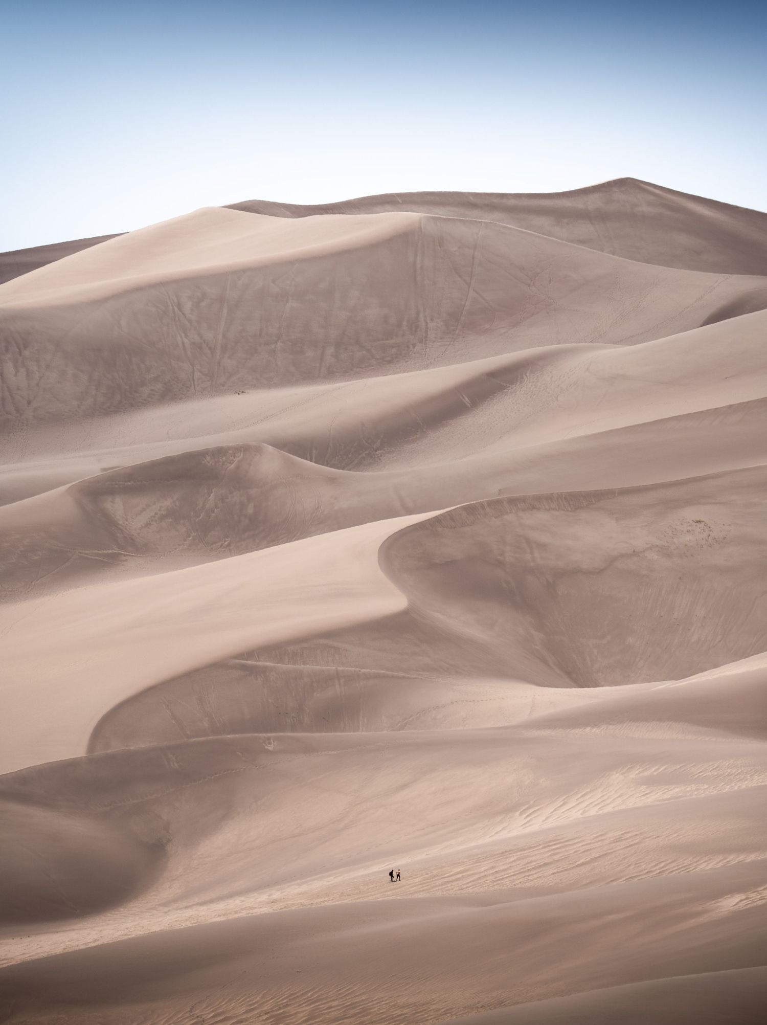 Two people stroll across the sand in Great Sand Dunes National Park in Colorado.