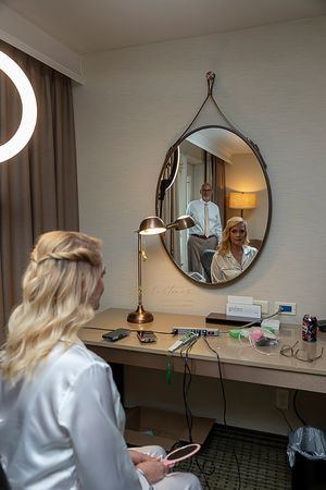 Bride getting ready looking in mirror with groom's reflection ©Milestones Studios