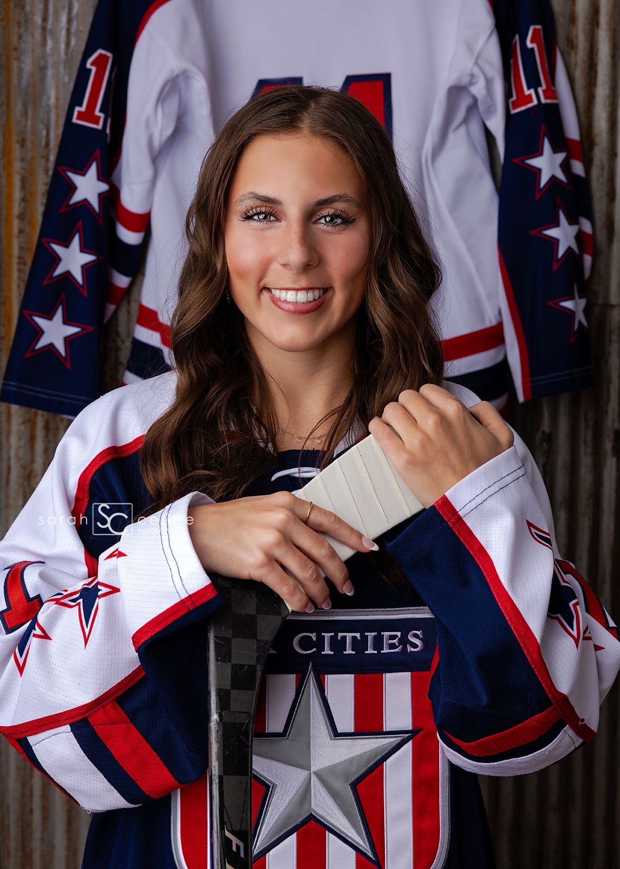 Young female hockey player in white Stars and Stripes jersey holding a stick, posing for a team portrait photo.