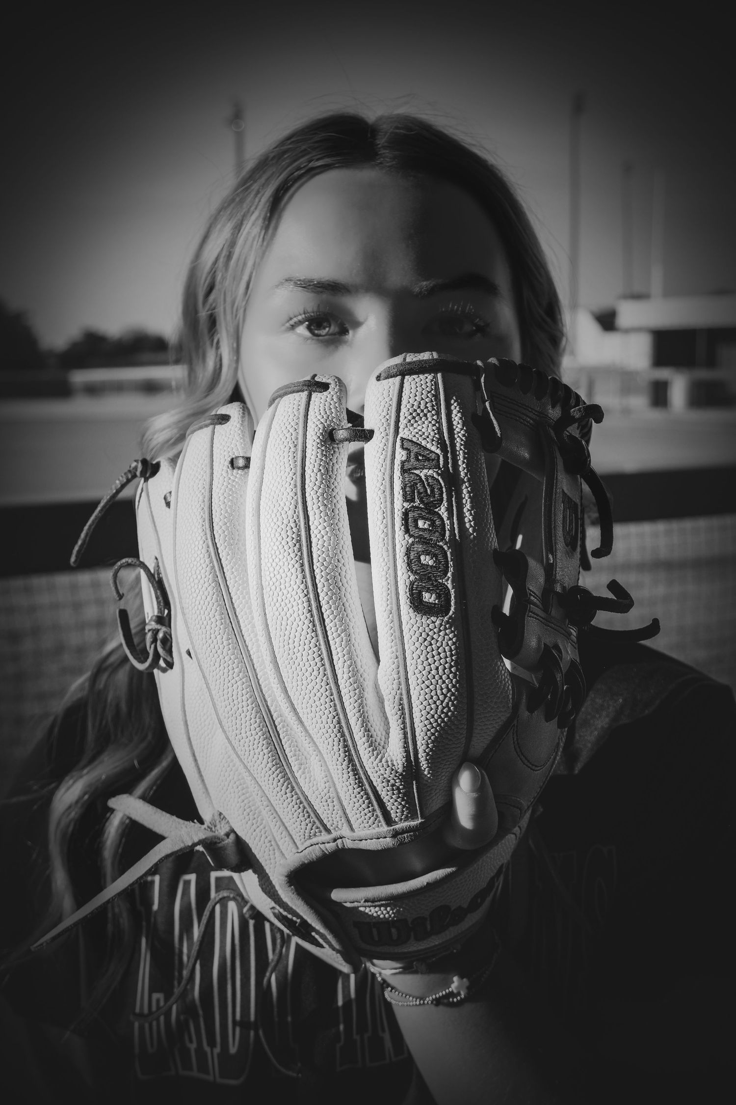 Black and white photo of a softball player holding a Wilson A2000 glove up to her face on a field.