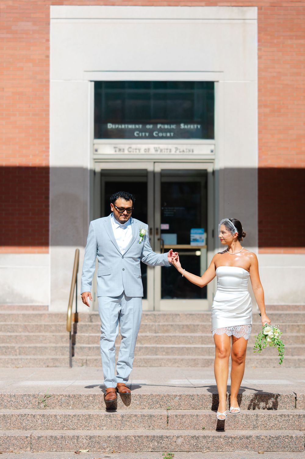 Bride and groom holding hands walking down steps outside White Plains City Court on their wedding day.