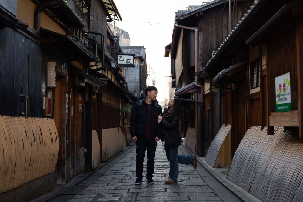 Couple holding hands while walking through a charming traditional Japanese stone-paved alleyway.