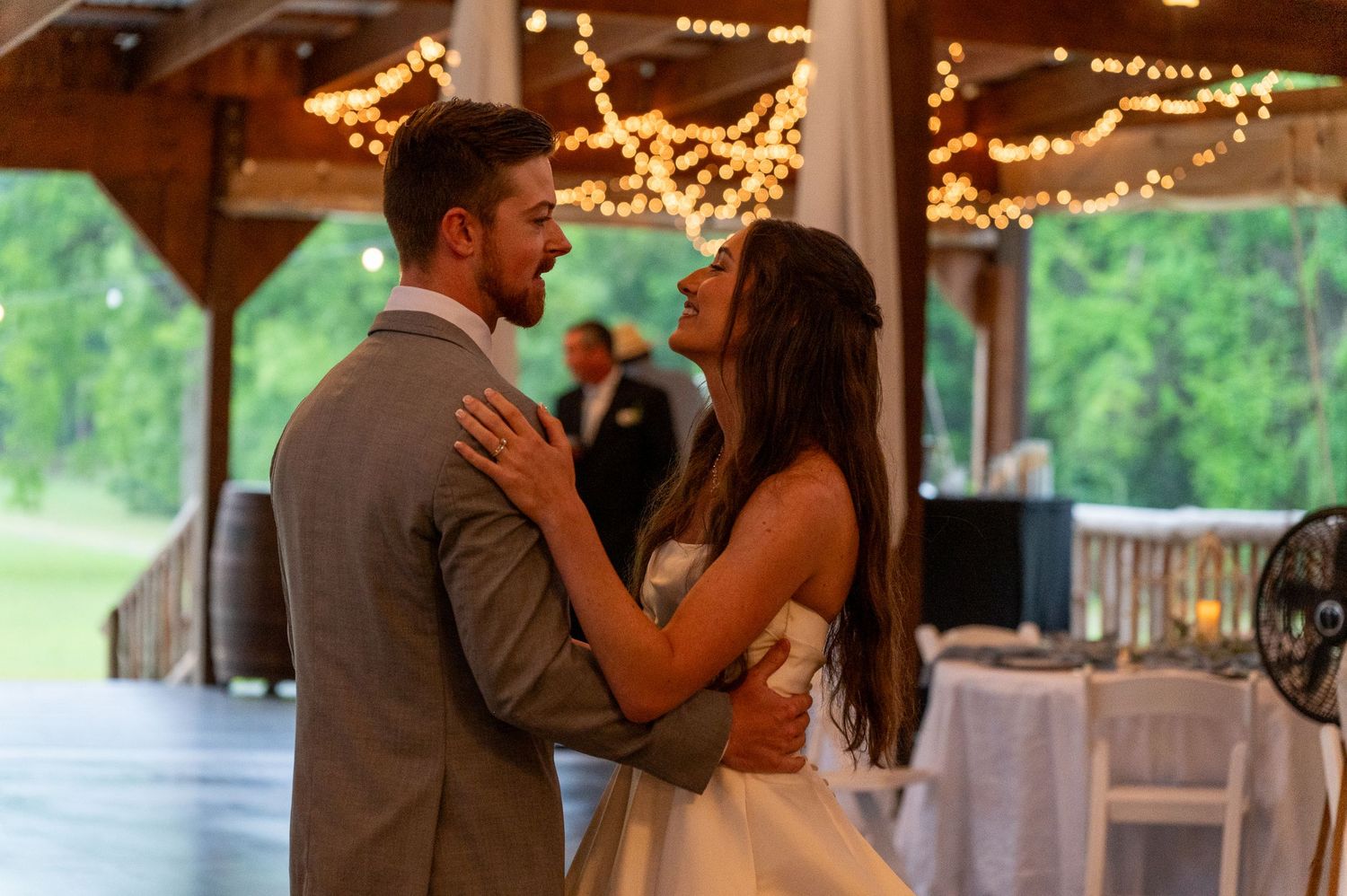 Bride and groom share their first dance under twinkling string lights at an outdoor wedding reception.