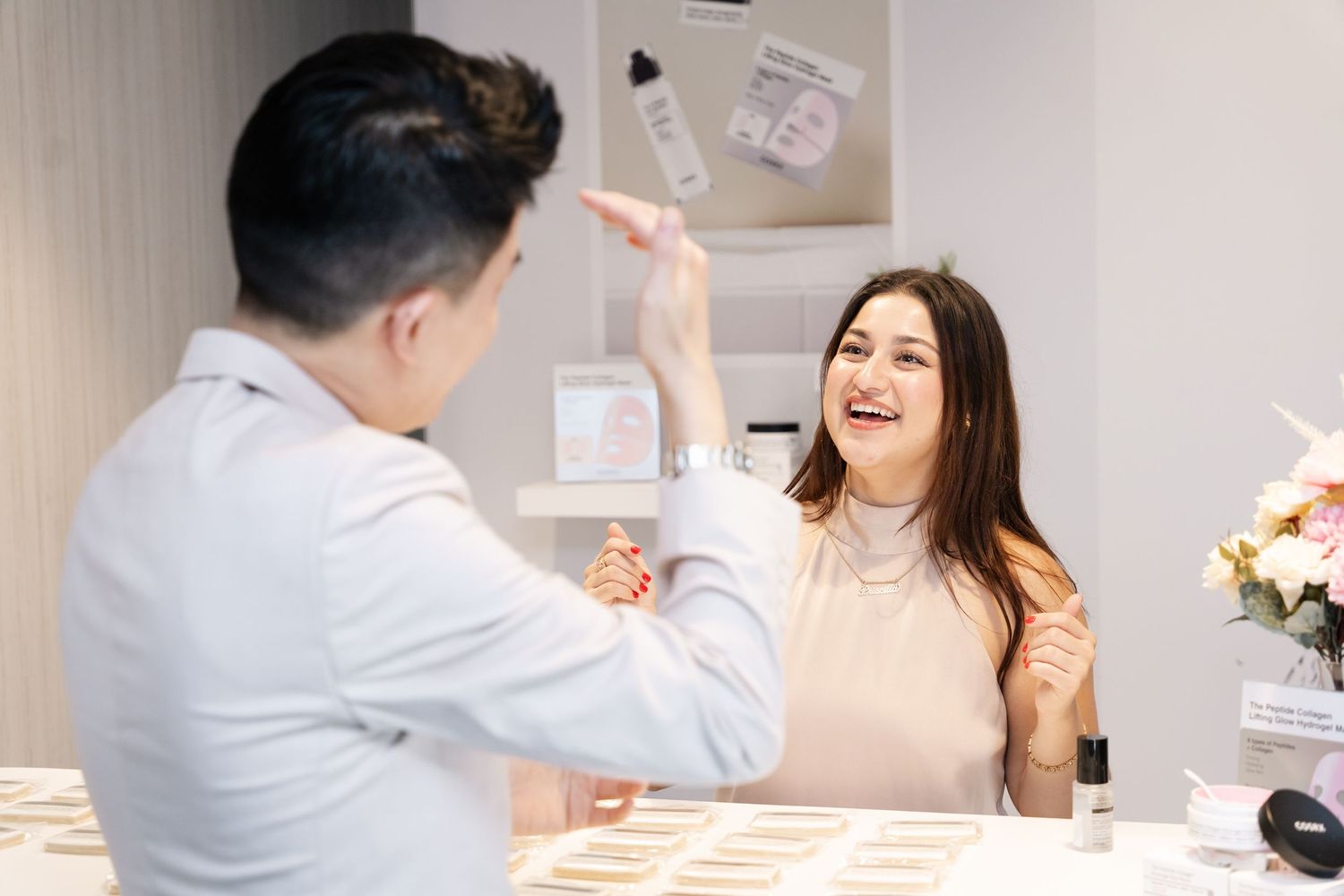 A woman laughs while high-fiving a man at a beauty counter in a bright skincare retail store.