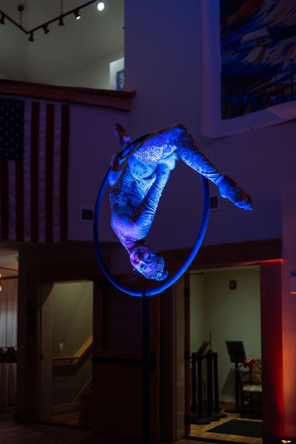 Aerial acrobat performing a stunning hoop routine under blue UV lighting at an indoor event venue.