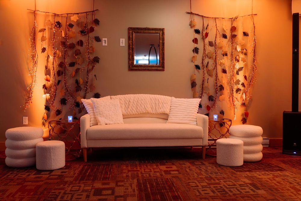 Elegant white sofa with round ottomans flanked by floral drapes and warm uplighting in an event space.