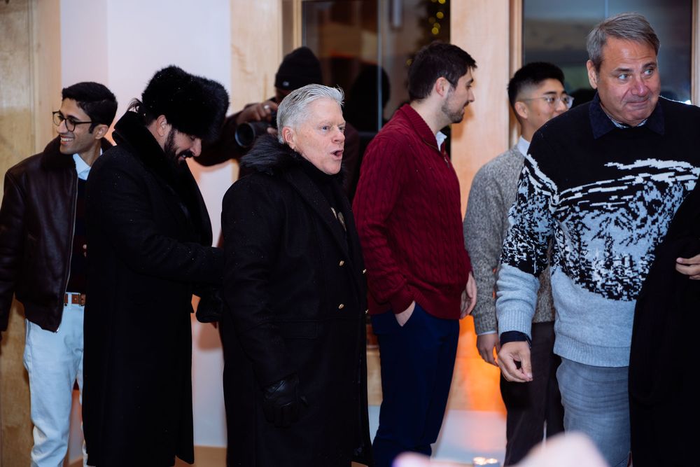 Group of people standing in line outside a venue wearing winter coats at a social event.